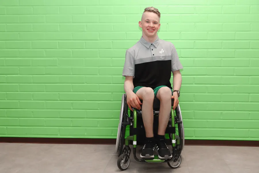 Henri Kössö hymyilemässä kameralle vihreää tiiliseinää vasten.